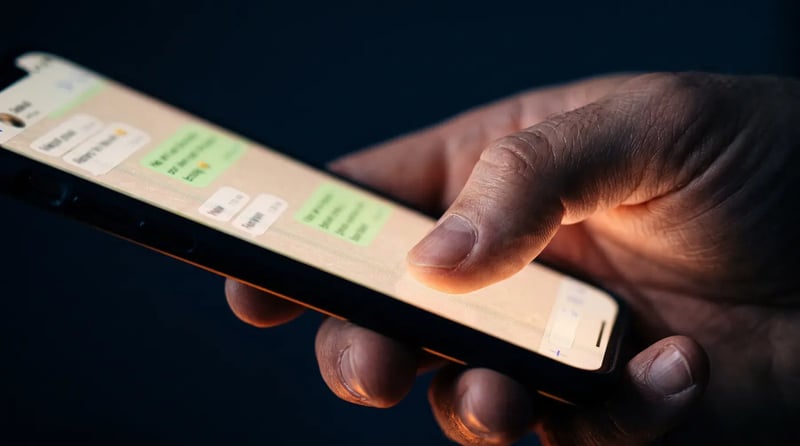Ένα χέρι κρατά κινητό με μια συνομιλία WhatsApp να φωτίζει την οθόνη